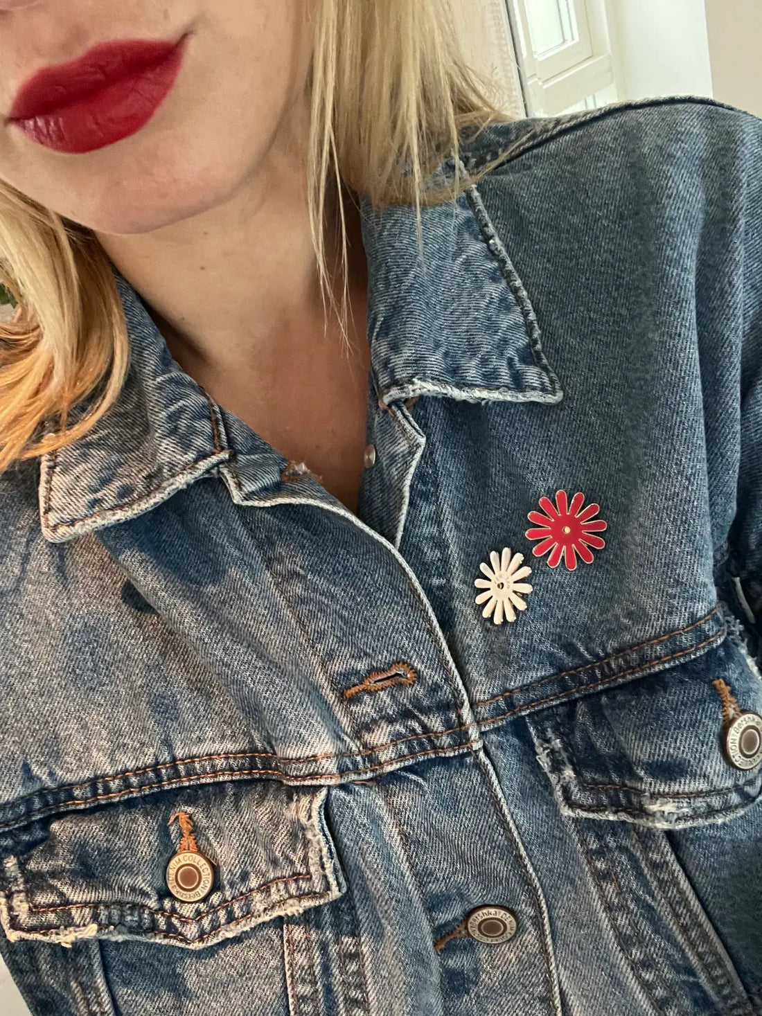 Femeie purtând geacă de blugi decorată cu insigne în formă de floare Femi.Eko®, una albă și una roșie, simbol al feminității și solidarității.