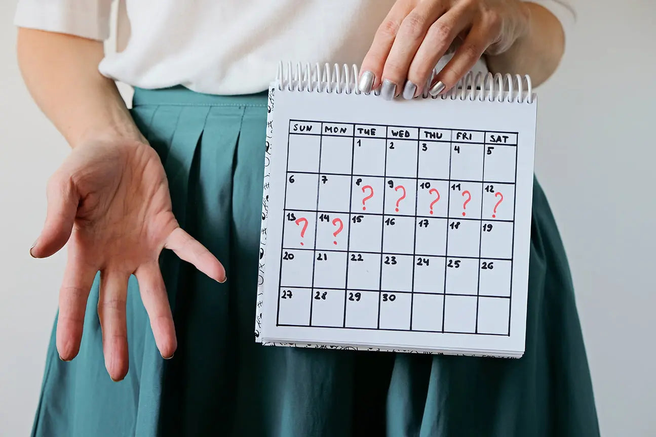 Femeie ținând un calendar cu semne de întrebare pe perioada estimată a menstruației, exprimând incertitudinea legată de ciclul menstrual.